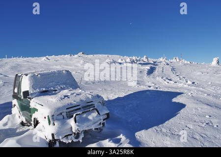 Terrain tout-terrain hivernal ensoleillé avec route alpine enneigée et voiture enneigée. Banque D'Images