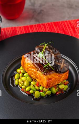 Filet de saumon grillé avec edamame et champignons shiitake, élégamment servi sur une assiette noire Banque D'Images