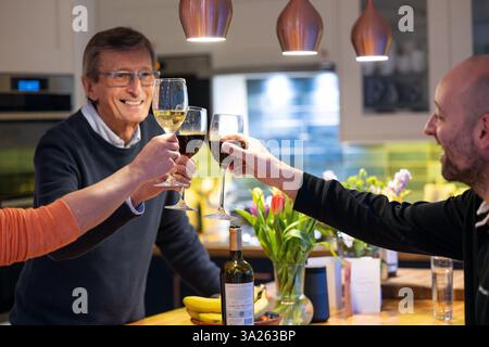 Homme souriant buvant du vin rouge avec des amis dans la cuisine. Banque D'Images