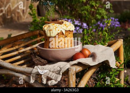 Gâteau de Pâques fait maison avec glaçage, cannelle et zeste d'orange, servi avec des œufs teints sur le lin dans un cadre naturel et rustique extérieur. Banque D'Images
