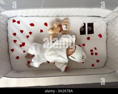Bébé nouveau-né dormant dans un berceau avec des coeurs et un ours en peluche Banque D'Images
