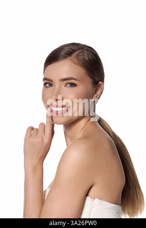 Jeune femme joyeuse affichant élégance et confiance avec un sourire radieux dans un fond minimaliste Banque D'Images