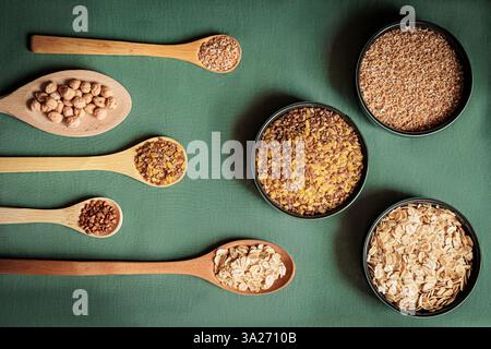 Composition à plat de divers grains et céréales dans des cuillères en bois et des bols sur un fond vert. Alimentation saine, aliments biologiques et nutrition conce Banque D'Images