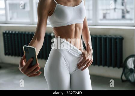 Vue rapprochée de la femme dans des vêtements de fitness blancs qui fait selfie avec le téléphone. Banque D'Images