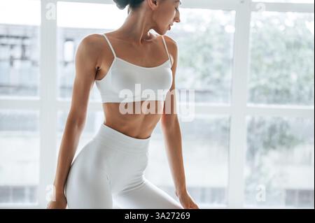 Femme en vêtements de fitness se tient debout contre la fenêtre avec vue. Banque D'Images