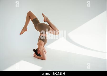 Utilisation de la tête debout. Jeune femme fait du yoga fitness à l'intérieur sur fond blanc. Banque D'Images