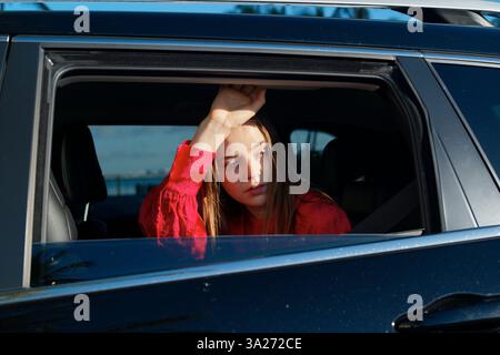 Femme en chemise rouge regarde soigneusement hors d'une fenêtre de voiture pendant la journée. Miami, Floride, États-Unis Banque D'Images