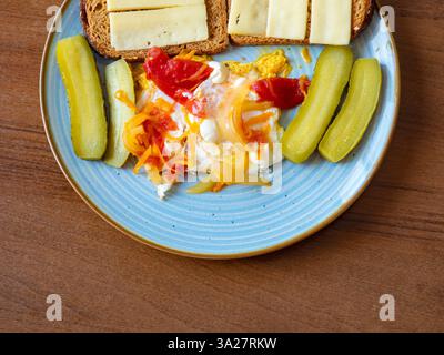 Un délicieux petit déjeuner met en valeur des œufs frits dorés nappés de fromage fondu, entourés de concombres marinés et de carottes croquants. Le presentati Banque D'Images