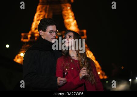 Un couple aimant profite d'une soirée romantique avec champagne sous la Tour Eiffel illuminée, célébrant l'amour, l'intimité et la magie de Paris la nuit. Banque D'Images