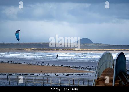 Dunbar, Royaume-Uni. 12 mars 2025. Un Kite surfer dans la baie de Belhaven près de Dunbar à l'extérieur d'Édimbourg, profite des vents violents du mercredi 12 mars 2025. Météo britannique le célèbre 'Bridge to Nowhere' peut également être vu dans le cadre, dans une partie de l'estuaire. Crédit image : Rob Gray/Alamy Live News Banque D'Images