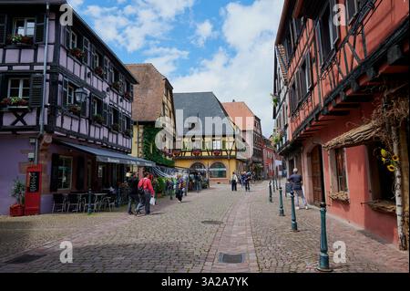 Kaysersberg, France - 15 juin 2024 : les visiteurs se promènent dans une étroite rue pavée bordée de maisons pittoresques et de boutiques à Kaysersberg. Banque D'Images
