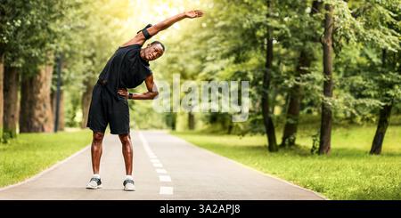 Sportif africain flexible s'étendant dans un parc public Banque D'Images