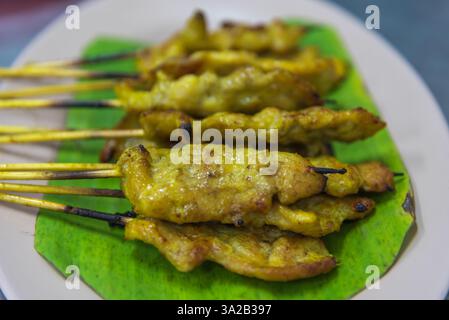 Satay de porc à la sauce aux cacahuètes servi avec des cornichons qui sont des tranches de concombre et des oignons au vinaigre au marché thaïlandais de Street food ou au restaurant à Bangkok T. Banque D'Images