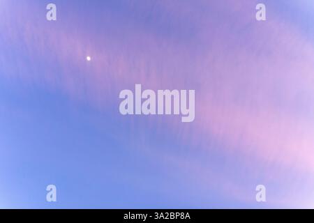 Des tons roses et bleus doux s'étendent à travers le ciel du soir, avec un délicat croissant de lune jetant un œil à travers les nuages doux. L'atmosphère tranquille sugg Banque D'Images
