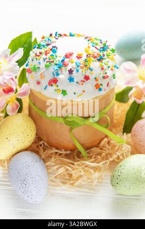 Gâteau de Pâques décoré de pépites colorées et noué avec un ruban vert entouré d'œufs et de fleurs de couleur pastel Banque D'Images