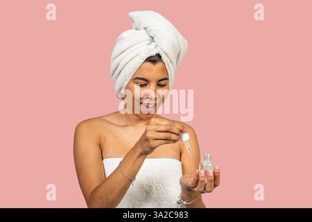 Femme heureuse portant une serviette appliquant l'huile essentielle sur le visage après la douche, beauté et concept de soins de la peau Banque D'Images