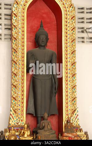 Statue de Bouddha noir dans le temple de Bangkok, encadrée par des motifs dorés ornés et de plus petites figures de Bouddha noir à la base Banque D'Images
