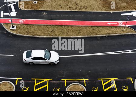Vue aérienne d'une berline blanche conduisant sur une route nouvellement pavée avec des pistes cyclables marquées et du ruban de construction jaune Banque D'Images