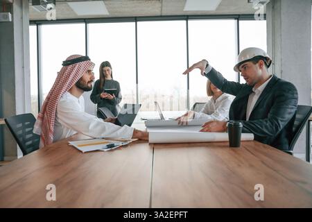 Vue latérale. Homme d'affaires musulman en tenue traditionnelle avec des collègues au bureau. Banque D'Images