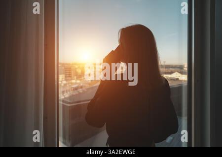 Silhouette d'une femme parlant au téléphone par la fenêtre du bureau. Banque D'Images