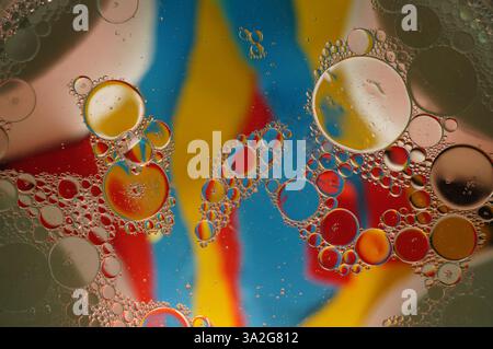 Macrophotographie abstraite de gouttelettes d'huile en suspension dans l'eau, créant un motif fascinant de bulles. Le fond vibrant de rouge, bleu et jaune Banque D'Images