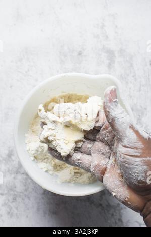 le beurre et la farine sont mélangés dans un bol blanc, le beurre et la farine sont mélangés dans une pâte rugueuse, le beurre et la farine étant utilisés pour faire de la pâte à biscuits Banque D'Images