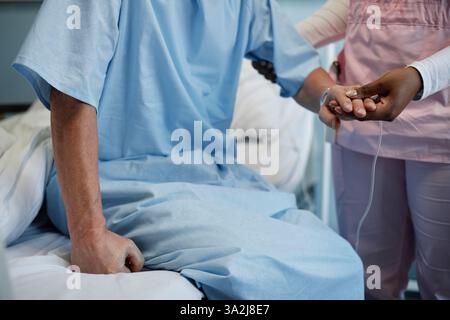 Agent hospitalier tenant la main du patient assis sur le lit de l'hôpital, offrant confort et soutien créant un moment de compassion dans un cadre médical Banque D'Images