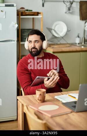 Un homme âgé élégant en tenue décontractée aime la musique avec des écouteurs tout en tenant une tablette. Banque D'Images