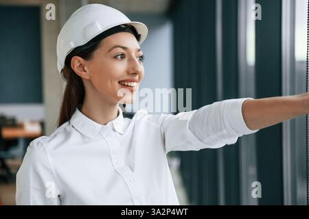 Pointant avec le doigt sur le côté. Architecte femme en casque et en vêtements blancs est à l'intérieur. Banque D'Images