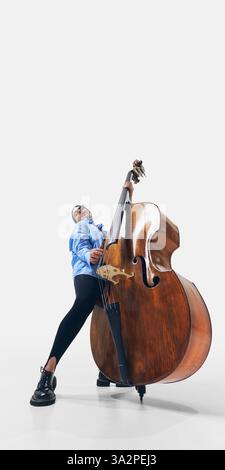 Bassiste féminine jazz élégante avec de longs cheveux coulants, embrassant le son et le rythme dans une expression musicale puissante sur fond blanc. Banque D'Images