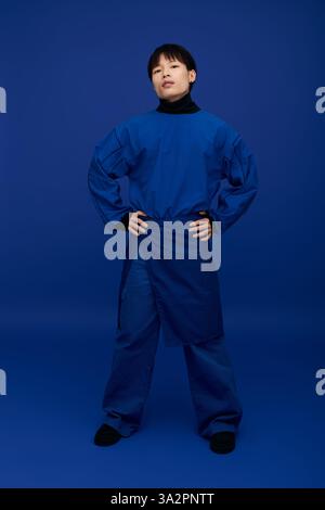 Confiant jeune homme asiatique pose avec les mains sur les hanches, affichant sa tenue bleue frappante. Banque D'Images