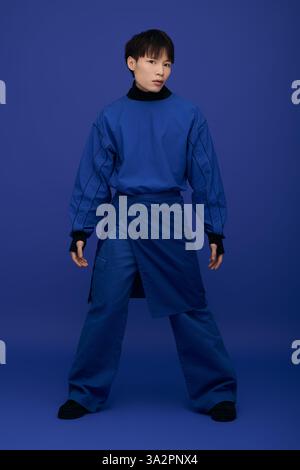 Un jeune homme dans une tenue bleue se tient confiant avec une pose élégante et une expression engageante. Banque D'Images