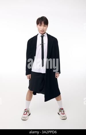 Un beau jeune homme asiatique modèle en toute confiance une tenue frappante dans un studio lumineux. Banque D'Images