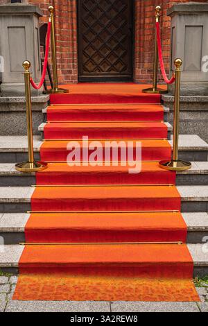 Tapis rouge sur les marches devant la vieille porte en bois du bâtiment Banque D'Images