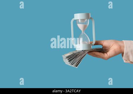 Femme tenant sablier avec de l'argent sur fond bleu Banque D'Images
