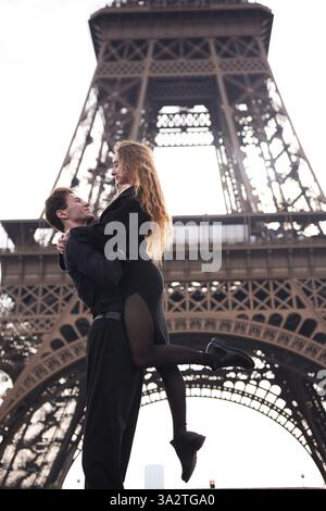 Un couple romantique partage un moment intime à Paris. L'homme élève la femme dans une étreinte aimante sous la Tour Eiffel, symbolisant la passion, la connexion et la magie de l'amour. Banque D'Images
