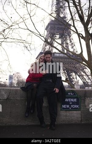 Un jeune couple partage un moment de calme sur une corniche de pierre de l’avenue de New York, avec la Tour Eiffel derrière eux. Banque D'Images