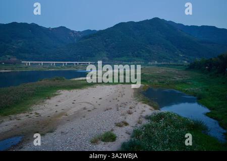 Comté de Gurye, Corée du Sud - 3 octobre 2021 : la rivière Seomjin serpente à travers la vallée alors que le crépuscule s'installe sur la rive sablonneuse. Vega luxuriant Banque D'Images