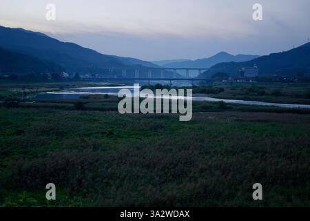 Comté de Gurye, Corée du Sud - 3 octobre 2021 : la rivière Seomjin serpente à travers la vallée au crépuscule, reflétant le ciel qui s'estompe. Ponts distants et Banque D'Images