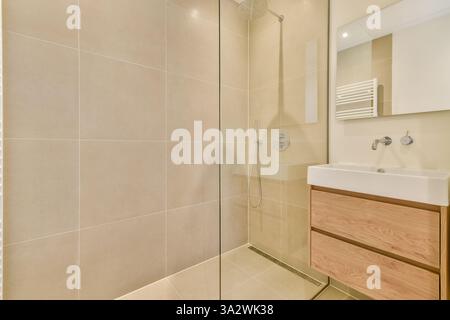 Cette élégante salle de douche moderne dispose d''une enceinte en verre, de carreaux élégants et d''un meuble-lavabo en bois. Il est conçu pour une vie contemporaine avec un mélange d'élégance et de fonctionnalité. Banque D'Images