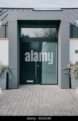 Une grande porte noire avec une fenêtre en verre au milieu. La porte est en bois et a une poignée argentée. La porte est en face d'un bâtiment avec un whit Banque D'Images
