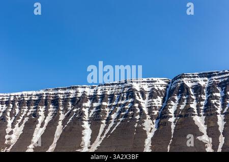 Crête de montagne de roche de lave enneigée avec couloirs à Isafjordur, Westfjords, Islande, avec ciel bleu en arrière-plan, espace copie. Banque D'Images