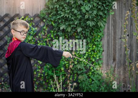 Garçon en costume de sorcier jetant un sort magique avec baguette à l'extérieur Banque D'Images