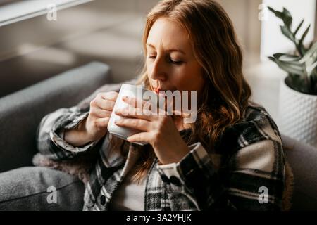 Une femme dans ses 40 ans profite d'une boisson chaude sur le canapé Banque D'Images