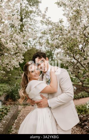 Mariée et mariée embrassent joyeusement sous les arbres en fleurs dans un jardin Banque D'Images