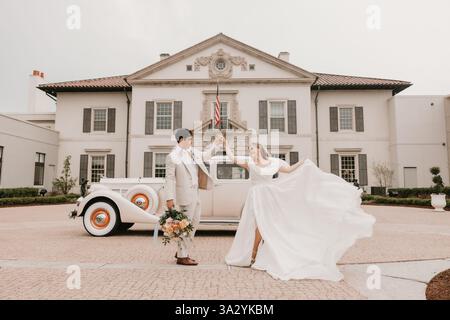 Mariée et mariée dansent joyeusement devant une voiture vintage et un manoir Banque D'Images