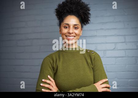 Femme confiante souriant en pull vert contre un élégant mur de briques Banque D'Images