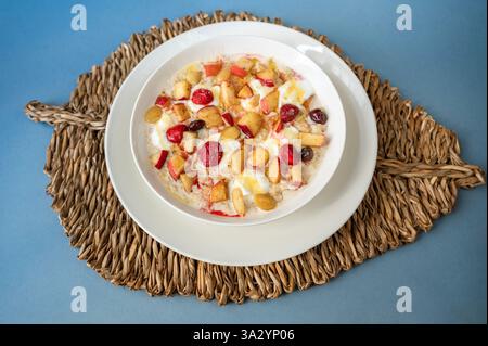 Bouillie d'avoine avec fraise, pommes cuites au four, amande et noix, miel et beurre dans une assiette sur tampon de bambou sur fond bleu. Banque D'Images