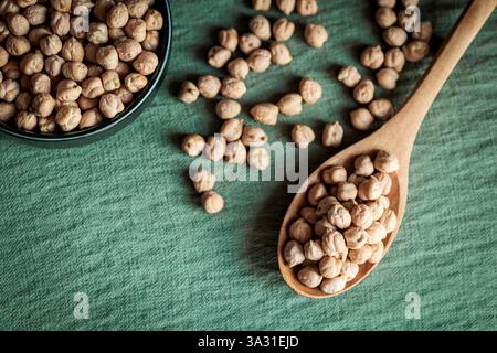 Vue de dessus de pois chiches séchés dans un bol en céramique et une cuillère en bois sur un fond vert, mettant en valeur des concepts alimentaires rustiques et sains Banque D'Images