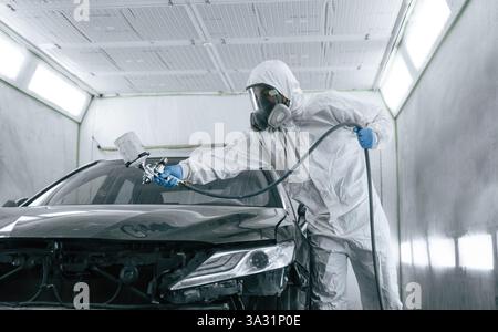 Vêtements de protection blancs. L'homme peint une voiture en utilisant un spray Guy. Banque D'Images
